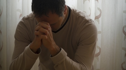 Un hombre orando al lado de su cama