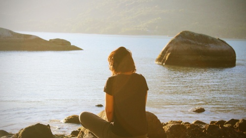 A woman sitting on a rock overlooking a body of water.